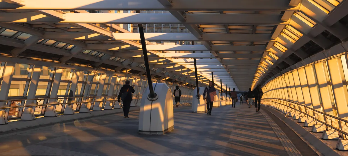 Passerelle couverte baignée par la lumière du soir, des piétons la traversent